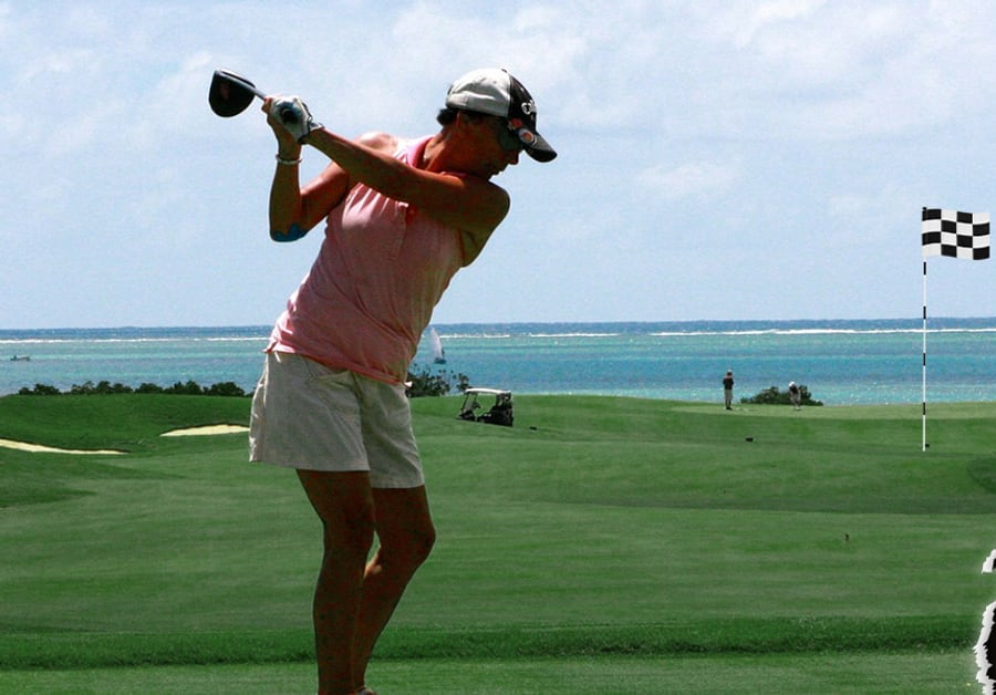 A golfer mid swing on a course by the water